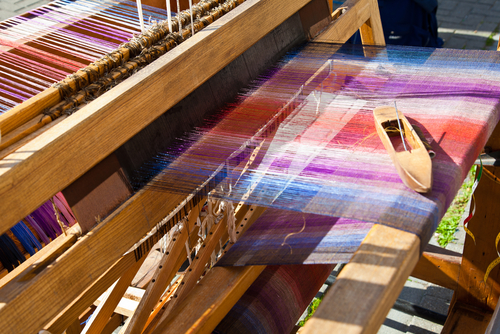 Colorful threads being woven on a loom.