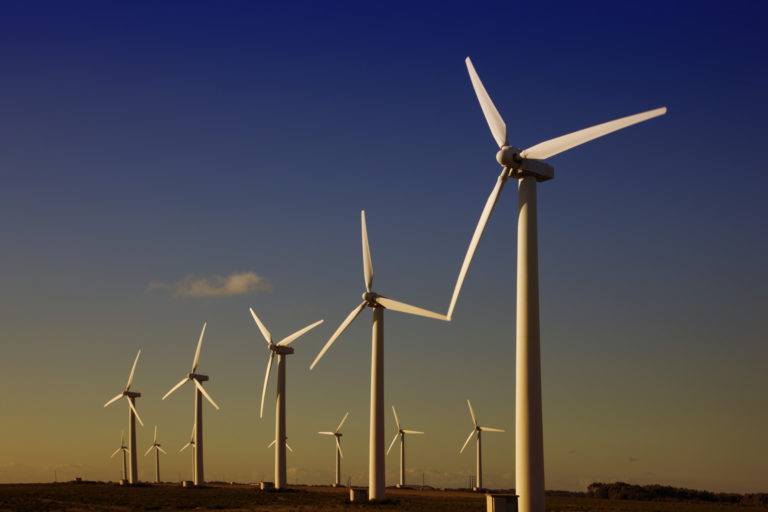 A row of wind turbines against a purplish blue skies.