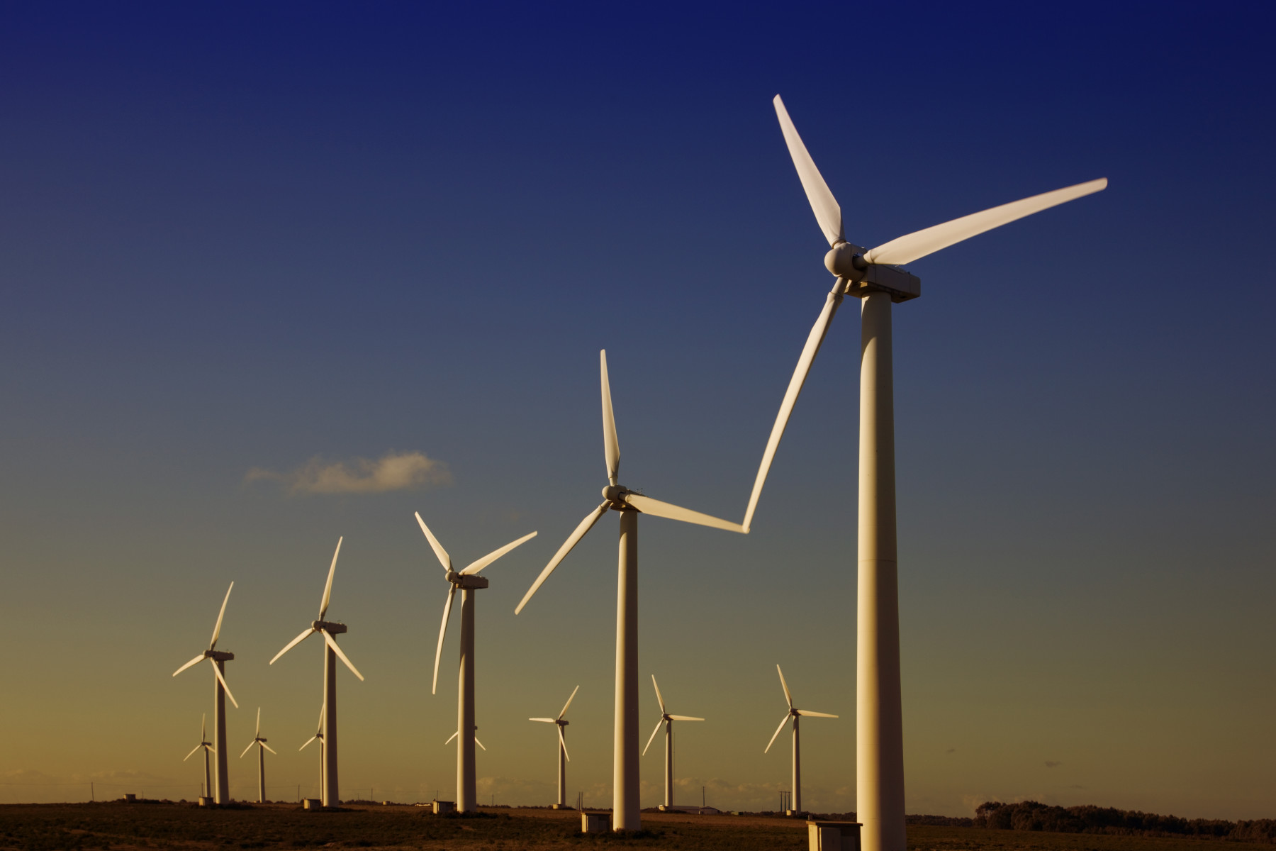 A row of wind turbines against a purplish blue skies.