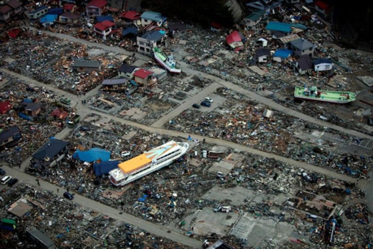 Aftermath of an earthquake and tsunami, with boats, buildings and debris strewn throughout the scene.