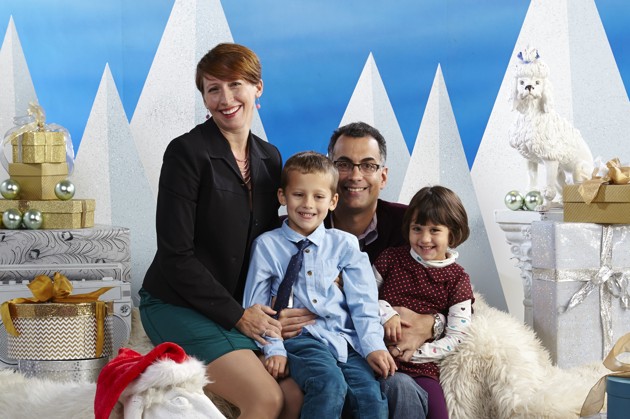 A family portrait with a man, a woman, and two young children in front of a holiday backgrop.