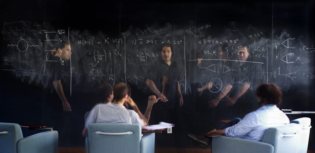 A multiple-exposure image of a man teaching in a classroom, moving in front of a blackboard.