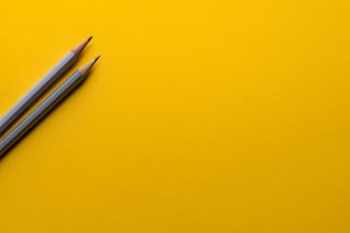 Two gray pencils sitting on a yellow surface.