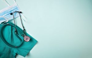 Full frame shot of face mask placed with stethoscope and medical scrubs. All are on green background.