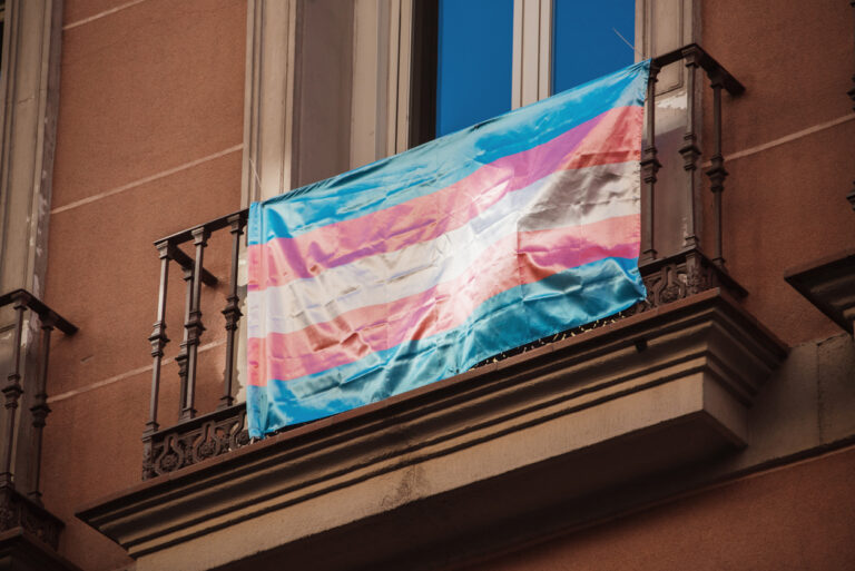 Transgender Pride flag hanging from a balcony.