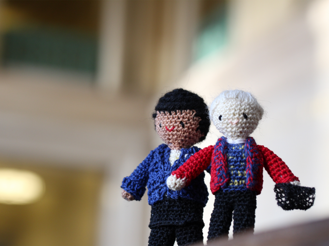 Two crocheted dolls, one with black hair and a blue sweater, and one with white hair and a red sweater.