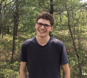 Eric Boodman standing in front of the camera, smiling, in a forest.