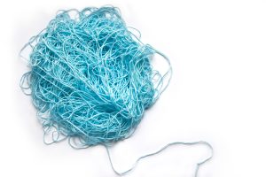 A tangle of blue yarn on a white background, with a single, orderly thread emerging from the lower right of the tangled ball.