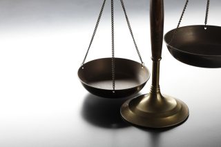A set of imbalanced bronze justice scales on a gray background.