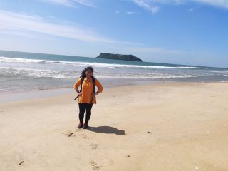 A woman stands, smiling and facing the camera, on an ocean beach.
