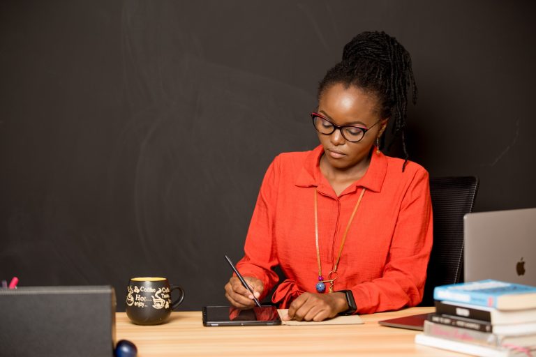 Verah Okeyo writes on a tablet while siting at her home-office desk.