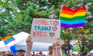 At a Pride parade, someone holds up a sign that says "Protect Trans Kids."