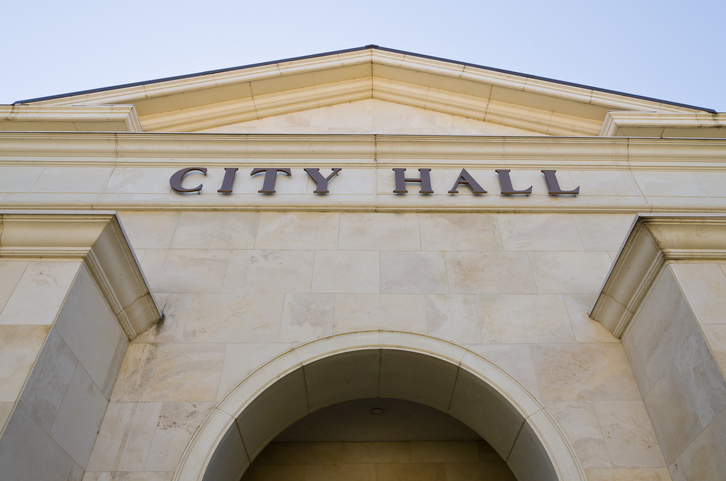Looking up at an imposing stone building with an arched doorway above which loom the words "City Hall" in capital letters.