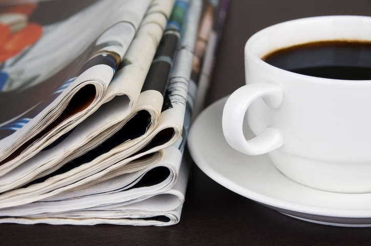 A stack of newspapers and a cup of coffee sit together on a table.