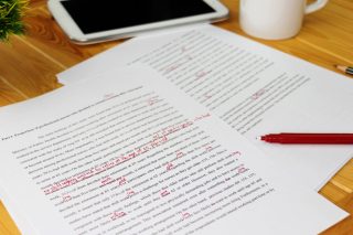 Pages of text edited with a red pen sit on a desk.