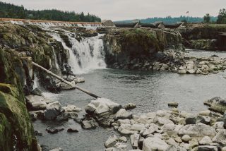 A wide-angle shot of Willamette Falls cascading down a large rock face into a deep pool.