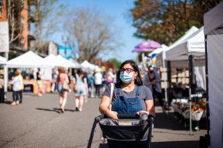 A woman wearing a mask pushes a stroller through an outdoor market.