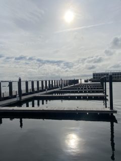 The sun shines down on an empty harbor through a thin shroud of clouds.