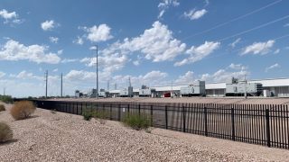 An outdoor shot showing part of a large one-story building surrounded by concrete, small stones, and a black fence.