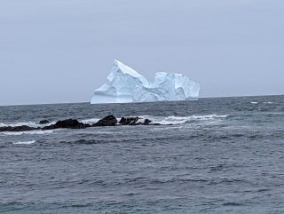 Looking out into the ocean with jagged rocks in the foreground and an iceberg on the horizon.