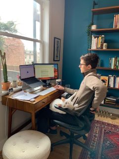 Tesla, a white cat, sits on Jonathan's lap while he works at his desk.