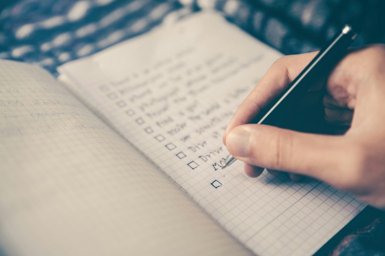 Close-up of a hand jotting a list in a notebook. The text is blurred and unreadable.