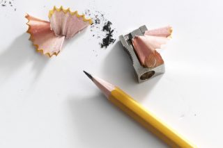A sharpened yellow pencil and sharpener with some pencil shavings scattered nearby.