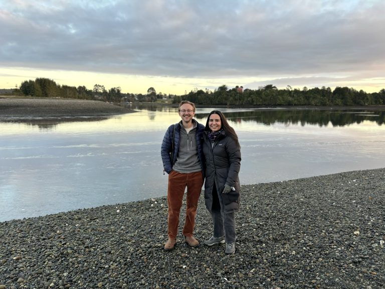 Christian Elliott and Muriel Alarcón stand next to each other on a stony riverbank.