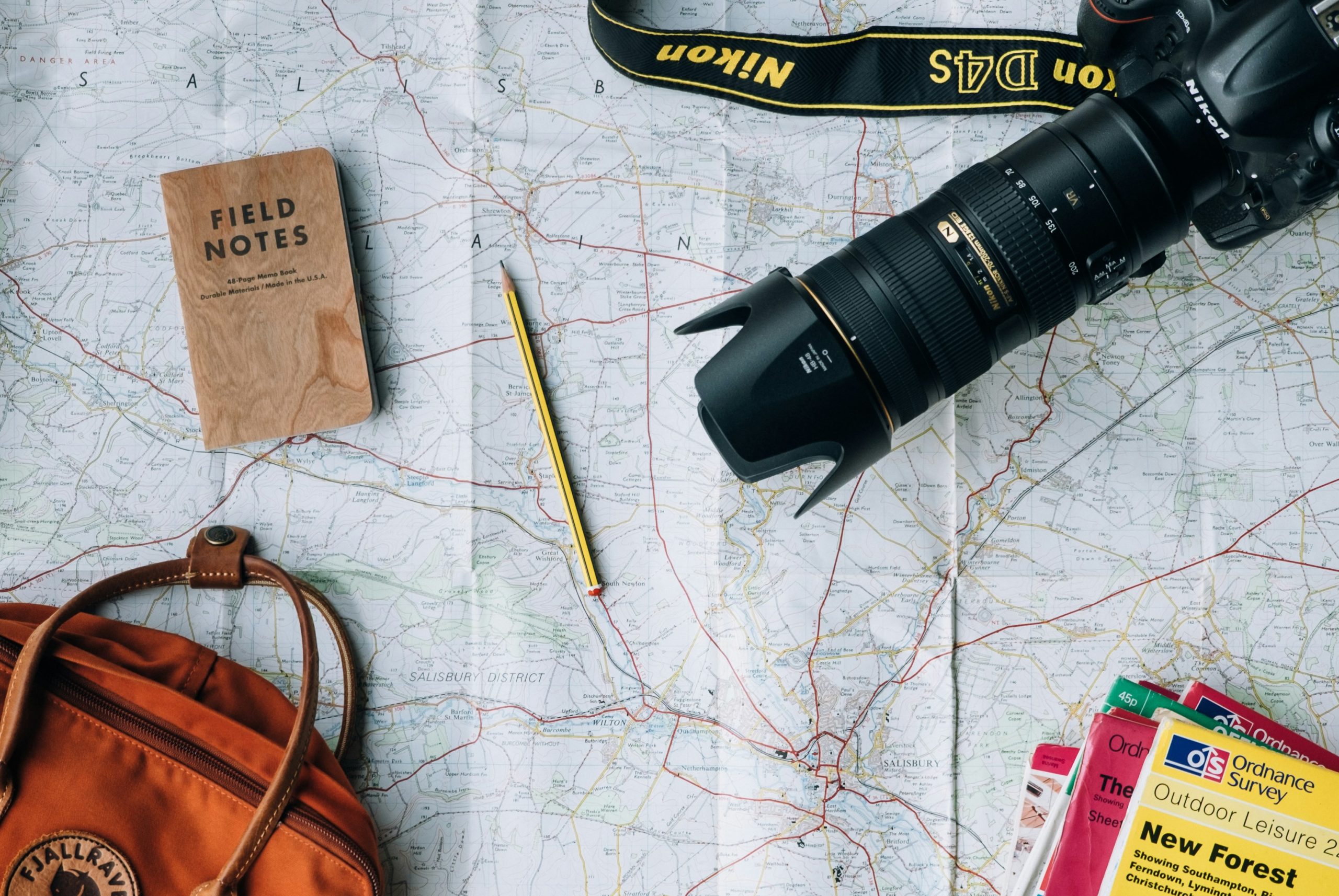 Map with backpack, pencil, camera, backpack, and guidebooks laid out on top.