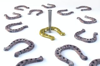 The image shows several grey horseshoes. In the middle is a gold horseshoe around a horseshoe stake.