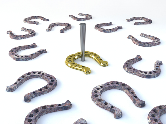 The image shows several grey horseshoes. In the middle is a gold horseshoe around a horseshoe stake.