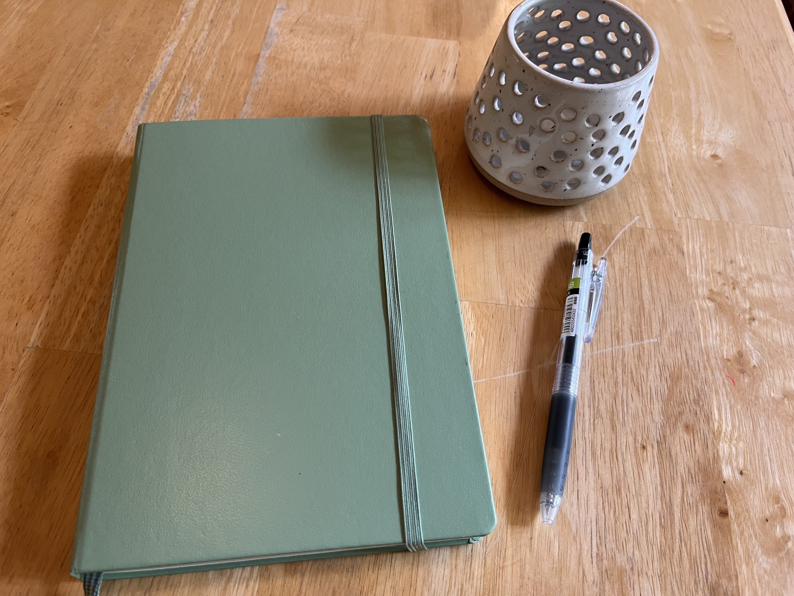 A green journal next to a pen and decorative vase