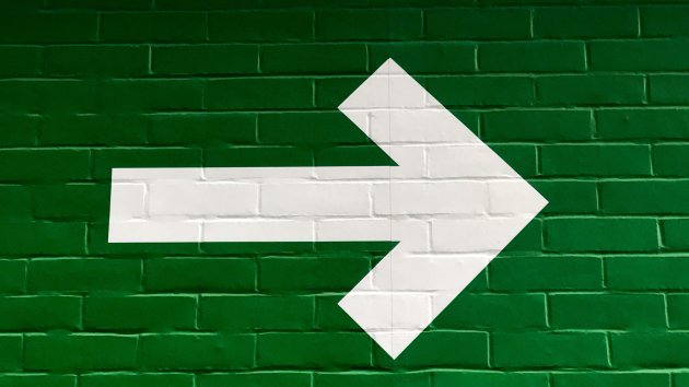 White arrow pointing to the right on a green brick background