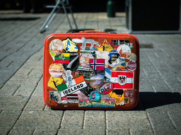 A red suitcase covered in stickers connoting world travel.